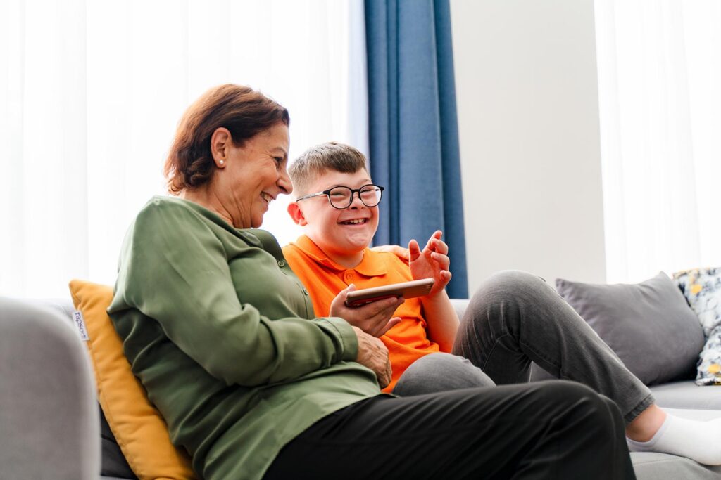 Boy with a disability with carer laughing and using a tablet