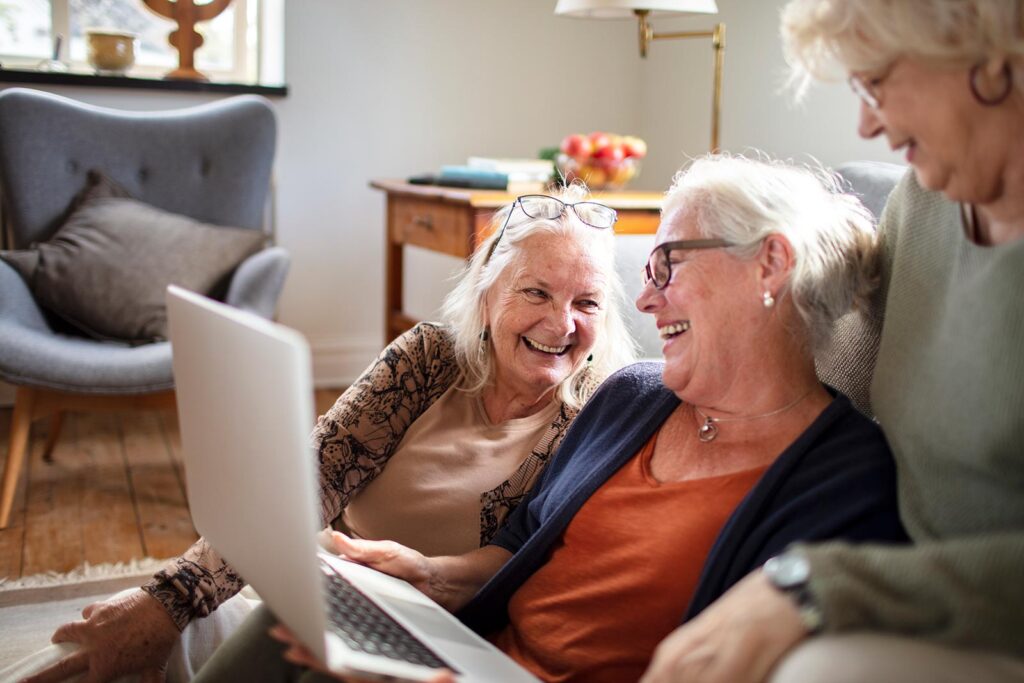3 older women at home laughing over a laptop