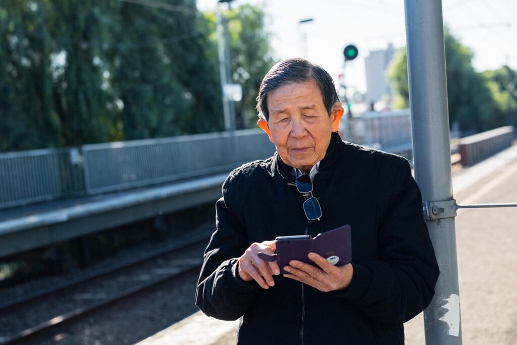 An older man looks at his phone at the train station