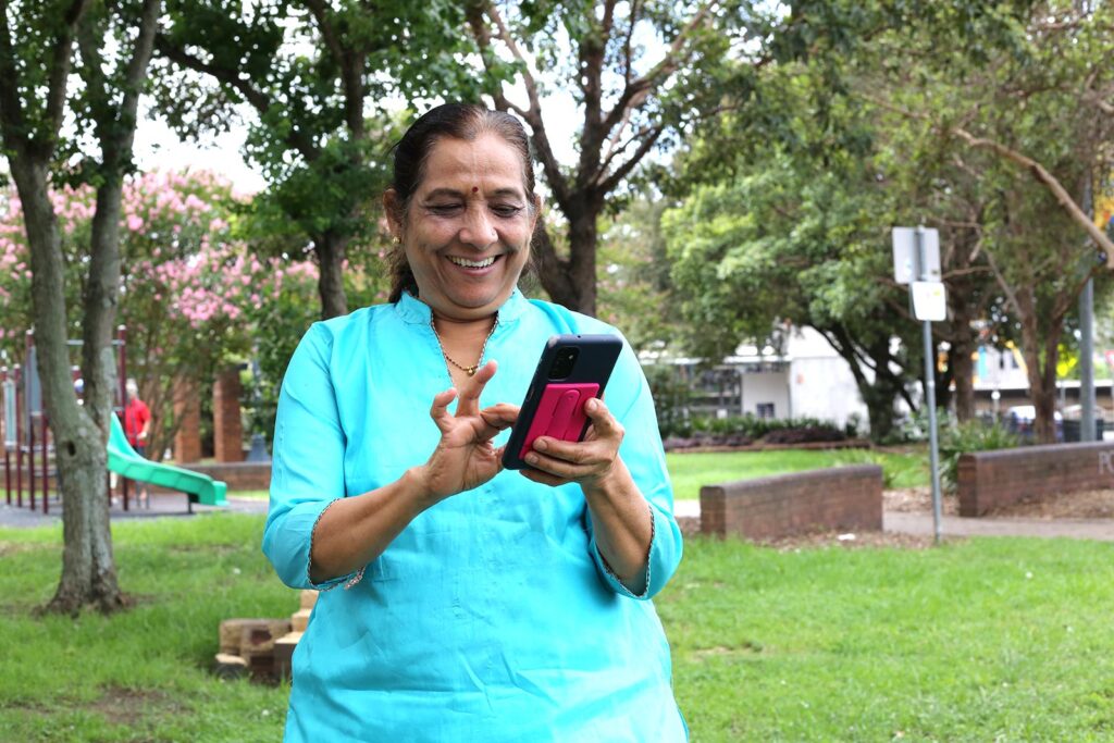 A woman outside smiles at her mobile phone