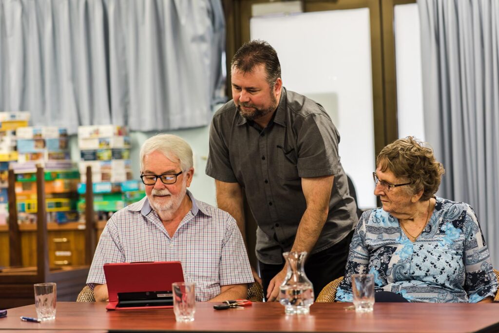 A women using a laptop being helped by a digital mentor. Another women is with them.